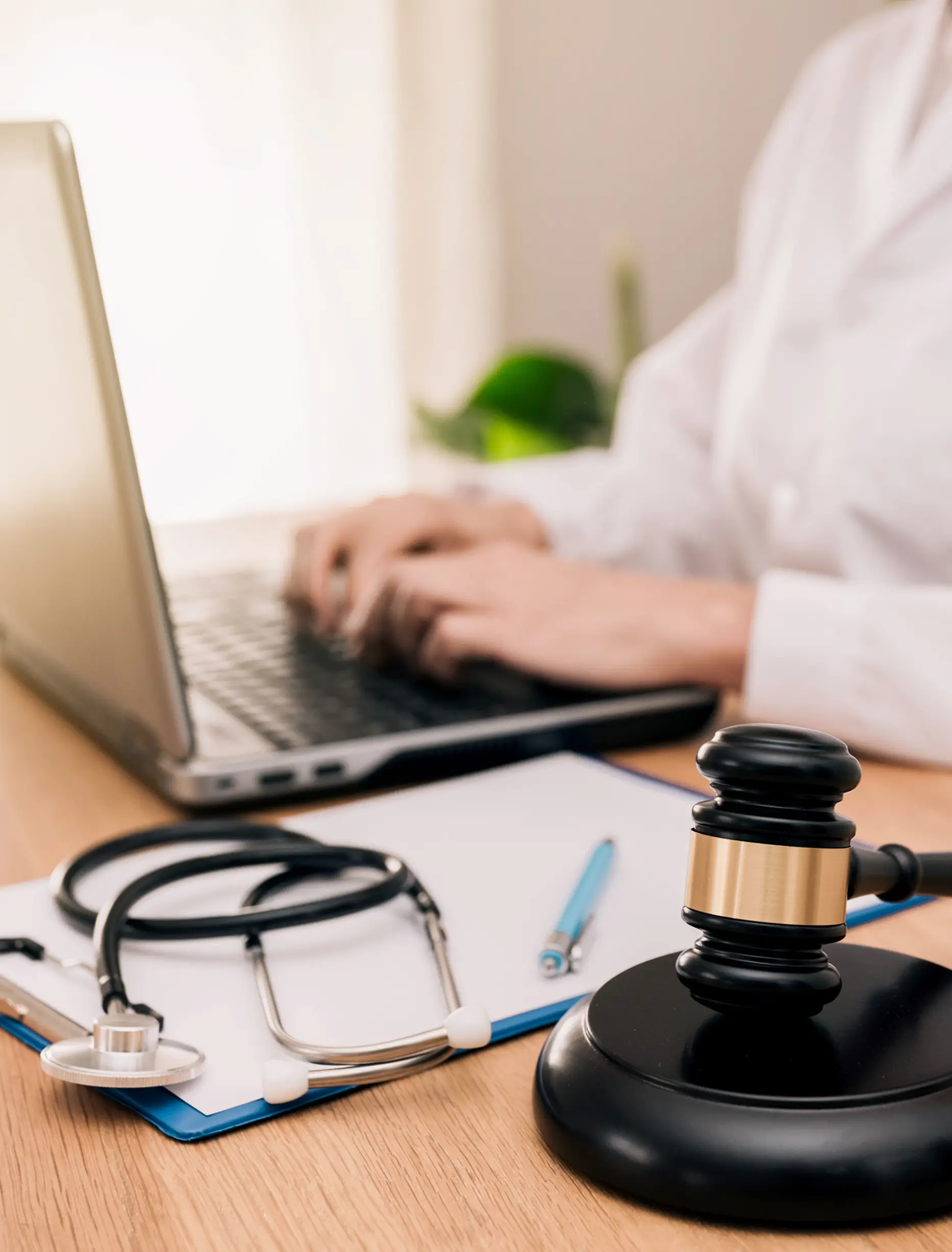 Laptop, gavel, stethoscope on desk, person typing.