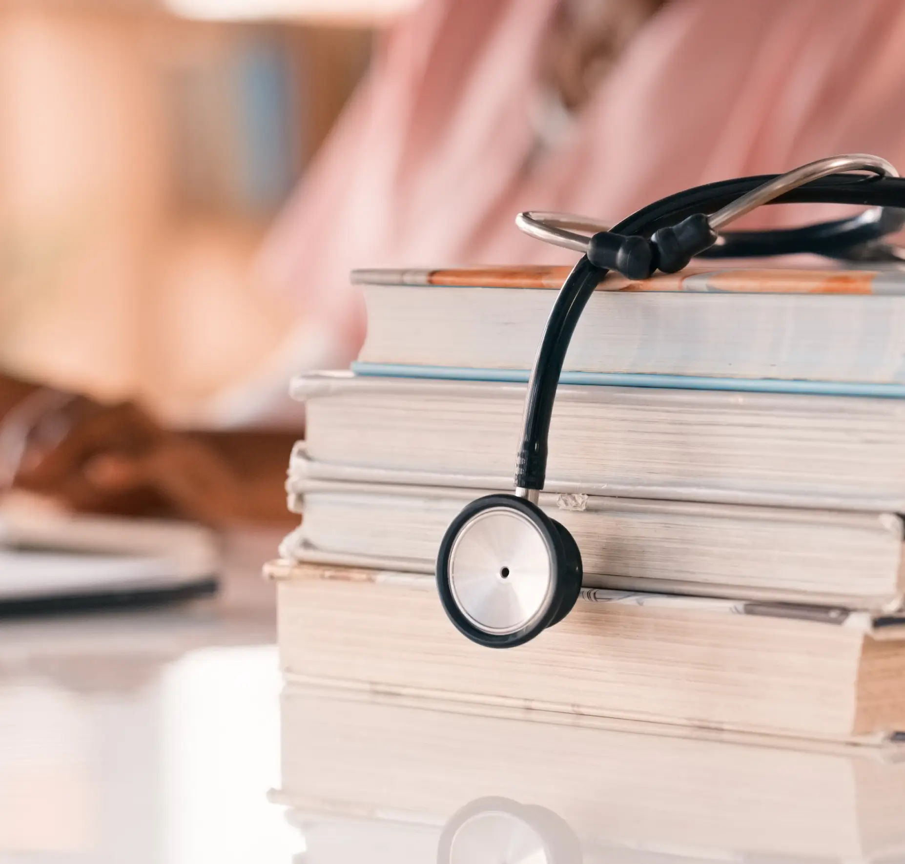 Stethoscope on stacked books, person in background.